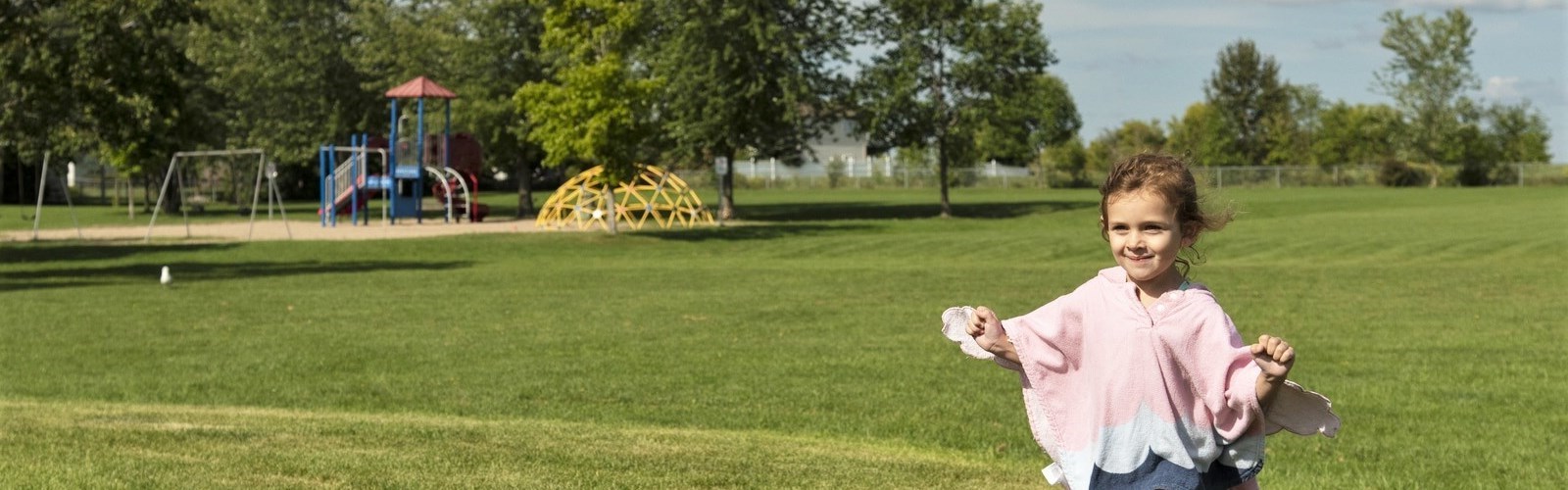 Young girl running in open field near playground equipment